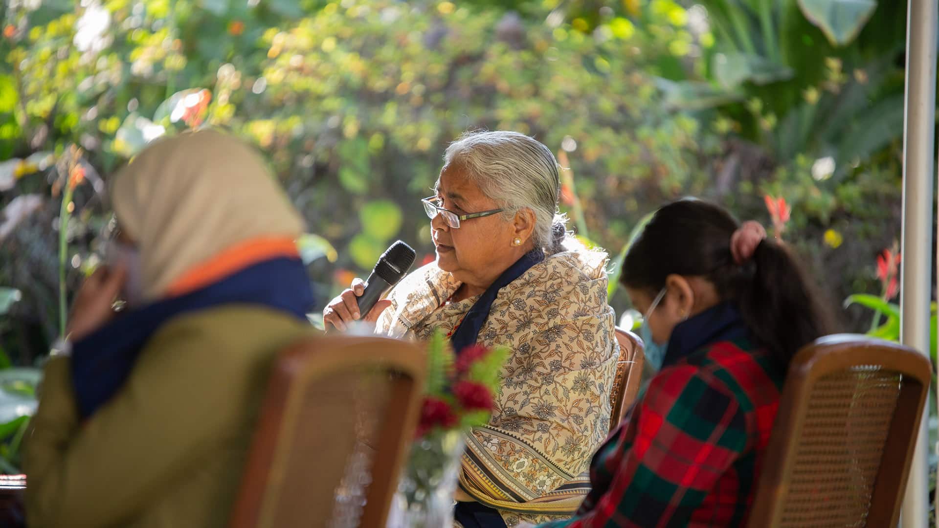 Sushila Karki, former judge and the first female interim prime minister of Nepal elected via Discord, at the Summit for Democracy organised by the US Embassy in Kathmandu in 2021. She is seated with a microphone in her hand next to two other women who are out of focus. In the background, the garden where the event is taking place.