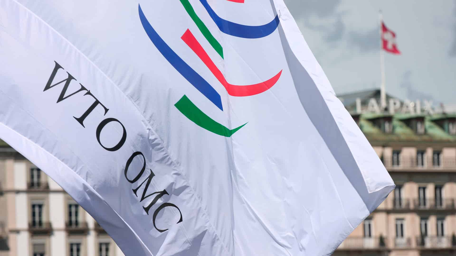 White flag with the logo of the World Trade Organisation (WTO) at its headquarters in Generva (Switzerland). The building has the the word “La Paix” on the roof and a Swiss flag flying.