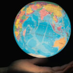 Mano sosteniendo un globo terráqueo iluminado con el océano Índico en el centro, rodeado por África, Asia y Australia, sobre fondo oscuro. Foto: Greg Rosenke (@greg_rosenke).