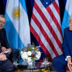 Javier Milei, his translator, and Donald Trump during the meeting between the two leaders at the Gaylord National Resort & Convention Centre in Oxon Hill, Maryland (22/02/2025). In the background, the flags of Argentina and the United States and a floral arrangement on the table in the centre.