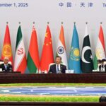 Main table at the plenary session of the 25th Meeting of the Council of Heads of State of the Shanghai Cooperation Organization (SCO) in Tianjin, China. In the centre, Xi Jinping (President of China) flanked by the other representatives and delegations. In the background, the flags of the SCO member countries, with text indicating the date (1 September 2025) and location (Tianjin, China).