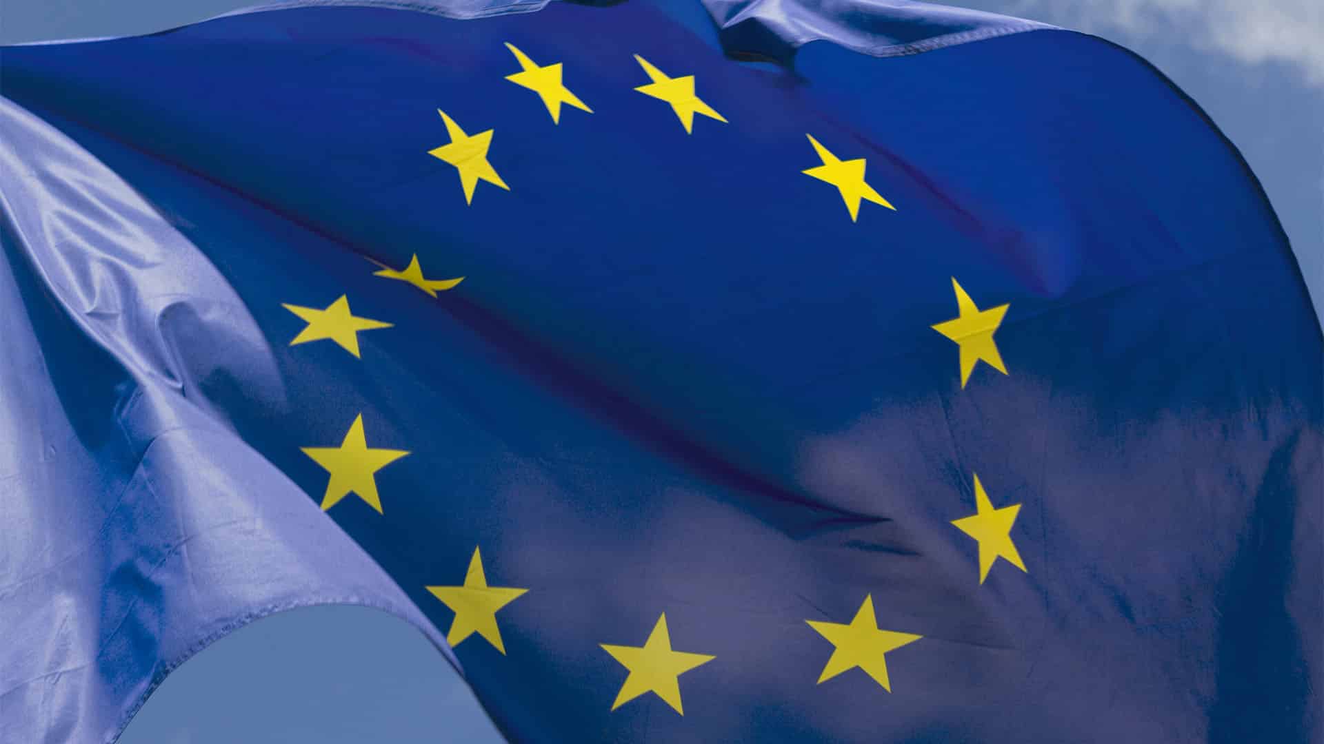 The flag of the European Union flies in the foreground against a clear, cloudless sky.