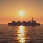 Buque cisterna de GNL al atardecer en el mar en Rusia (28/04/2020). Un cielo anaranjado muy vibrante ilumina la escena, que se refleja en el mar, en contraposición al buque cisterna, que aparece como una sombra sobre el agua.