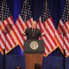 Donald Trump, presidente de EEUU, presenta la Estrategia de Seguridad Nacional de 2017 en el Ronald Reagan Building de Washington D.C. (18/12/2017). Trump, con gesto inquisitivo, está en el centro del del escenario tras un atril con el sello presidencial. Tras él, seis banderas estadounidenses y, al fondo, un telón azul oscuro. En 2025, no ha habido una presentación específica para el documento.