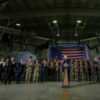 Donald Trump aplaude en su discurso ante las tropas tras una tribuna con el logo del presidente (25/04/2025). A su izquierda, lo acompañan en su visita: el secretario de Defensa, Pete Hegseth y autoridades militares y políticas de Míchigan. A su alrededor, los soldados y dos aviones de la base y, al fondo, una gran bandera de Estados Unidos. Están en una nave industrial de la Base Aérea de la Guardia Nacional de Selfrifge, Míchigan.