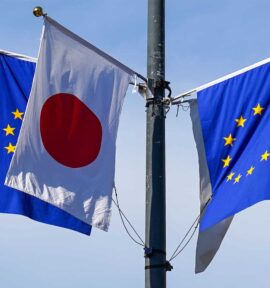 Mástil con las banderas de la Unión Europea y Japón, durante la visita de Kaja Jallas a Japón en julio de 2025. El mástil tiene cuatro postes con cuatro banderas, dos de la UE y dos de Japón. Detrás de las banderas, un edificio blanco con numerosas ventanas y un cielo completamente azul y despejado.