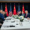 Reunión bilateral entre Donald Trump y Xi Jinping (30/10/2025) en el aeropuerto internacional de Gimhae, en Busán, Corea del Sur. A la izquierda, los representantes de la administración de China, liderada por Xi Jinping; y, a la derecha, la de EEUU, encabezada por Donald Trump, miran hacia la cámara que toma la fotografía. Al fondo, tres banderas de EEUU y tres de China, intercaladas.
