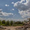 Bloque residencial partido por la mitad debido a los bombardeos en Kyiv. Al fondo, tras un terreno con vegetación y árboles, la cúpula y una torre doradas y blancas de una iglesia, se mantiene intacta. El cielo es claro, aunque con varias nubes.