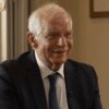 Josep Borrell sonríe en la grabación del vídeo por los 40 años de España en la Unión Europea en la sede del Real Instituto Elcano. Borrell está sentado delante de una ventana y al lado de un marco de color dorado, que ocupan parcialmente la imagen.