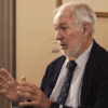 Miguel Arias Cañete conversa enfatizando con sus manos en la grabación del vídeo por los 40 años de España en la Unión Europea en la sede del Real Instituto Elcano. Arias Cañete está sentado delante de una ventana y al lado de un marco de color dorado, que ocupan parcialmente la imagen.
