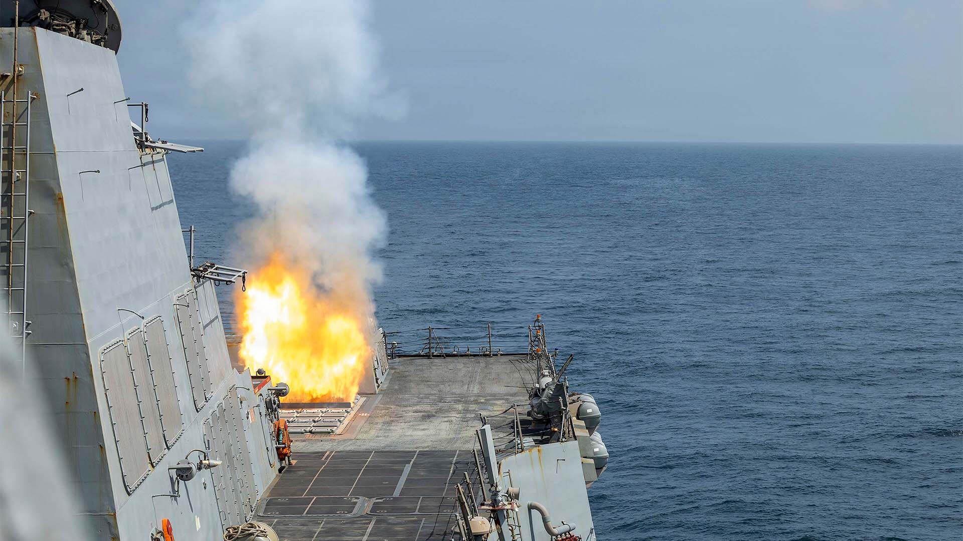 Vista parcial del buque de guerra estadounidense USS Delbert D. Black mientras lanza un misil Tomahawk, visible por el fuego que origina su salida. El buque forma parte del dispositivo de apoyo a la Operación Furia Épica (28 de febrero de 2026). El mar aparece completamente vacío y, al fondo, se ve un cielo claro y despejado.