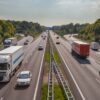 Coches y camiones circulan en ambas direcciones por la autopista A12, en Países Bajos. La mediana divide los carriles en ambos sentidos, y, a los costados, varias concentraciones de árboles. Al fondo, un cielo claro, con algunas nubes.